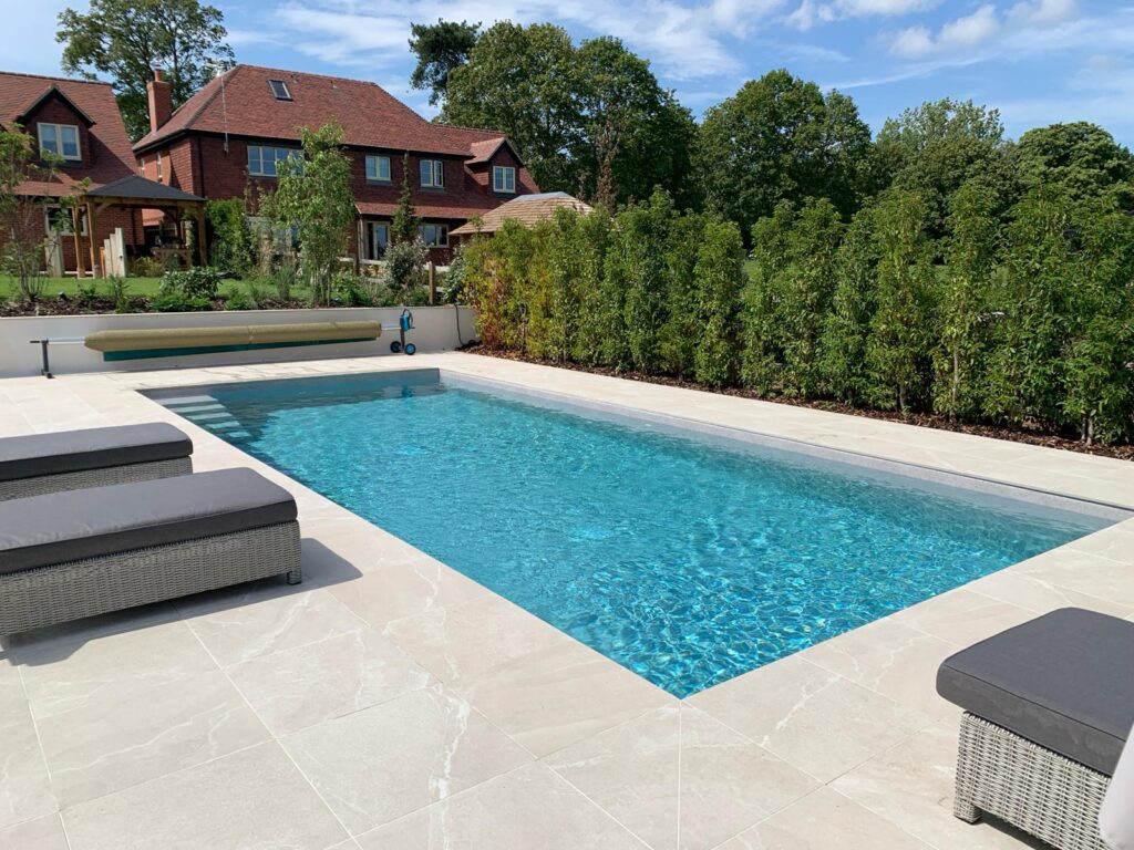 Luxury rectangular backyard swimming pool with light patio tiles and modern house.